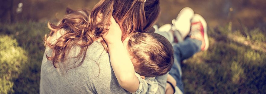Mother holding child in a loving warm embrace with dappled light by a river symbolising quiet joy after trauma. Learn more about parenting after hard seasons at www.shineom.com.au/podcast