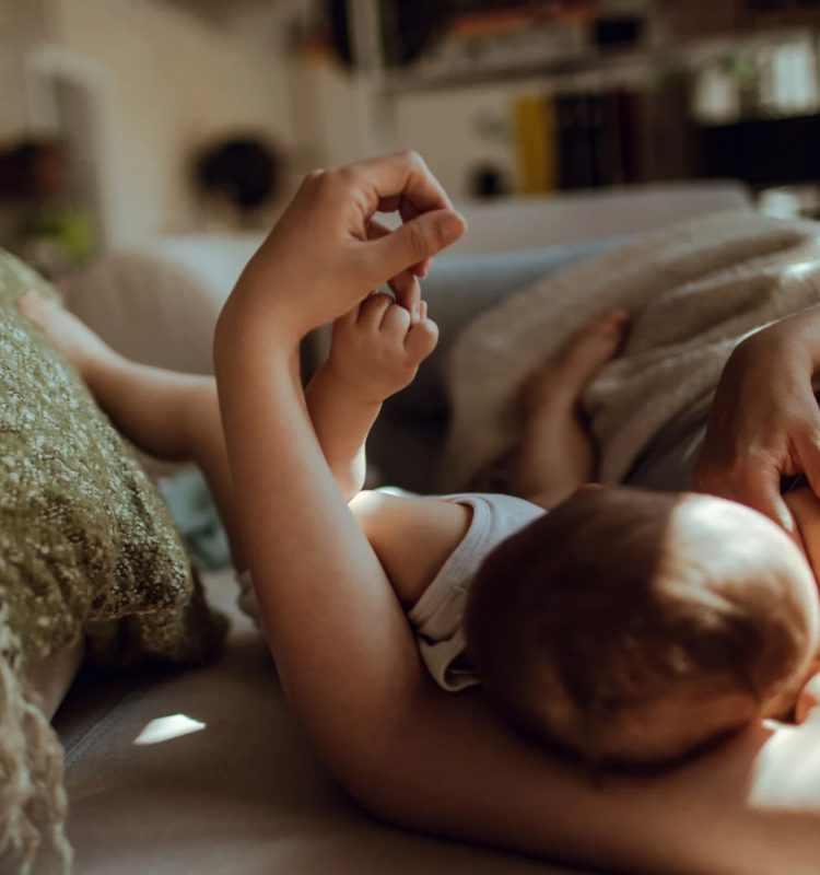 Mother holding and breastfeeding her child in a quiet moment of connection at home symbolising that joyful parenting can be found in the little moments. Learn more at www.shineom.com.au