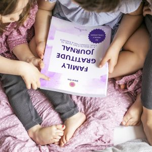 Children sitting closely together on a bed, holding and looking at the Family Gratitude Journal by Shine Om — a full-colour mindfulness workbook for families promoting calm, connection, and kindness. Visit www.shineom.com.au to learn more.