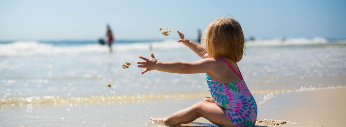 toddler girl sitting on shore during day